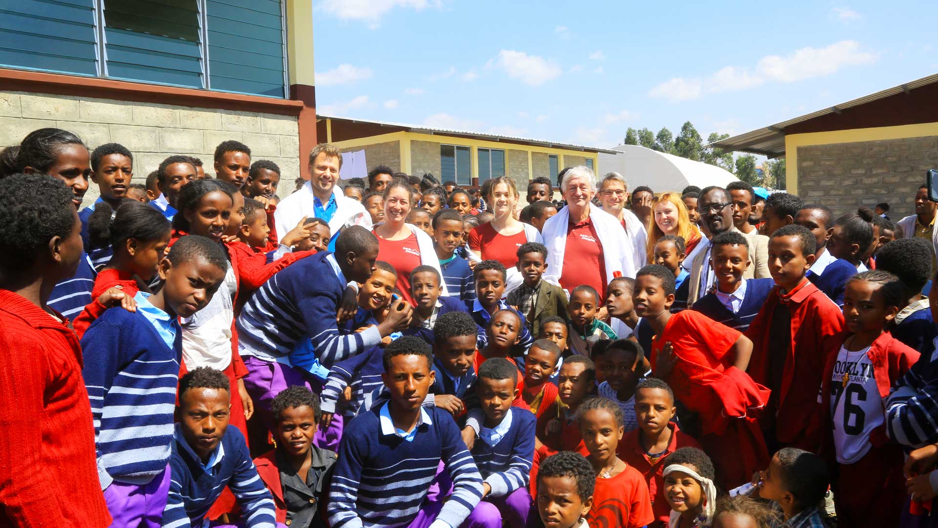 Eine Gruppe von Schulkindern und Lehrenden in traditionellen Gewändern steht vor der neu errichteten Schule in Ginchi.
