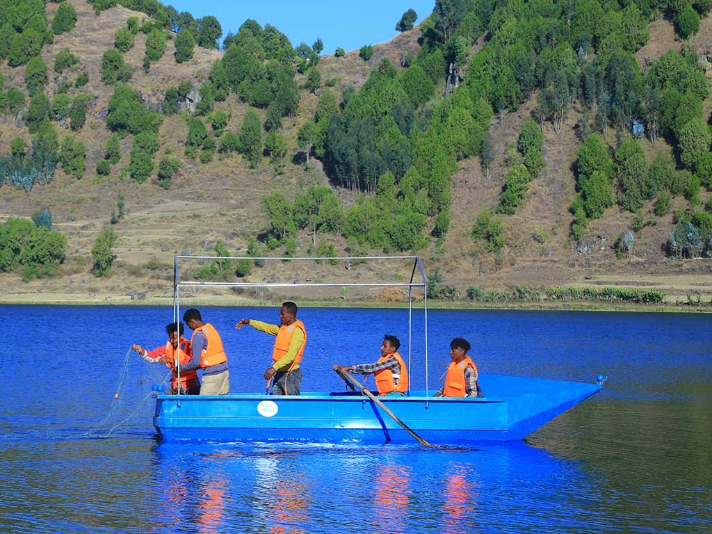 Einige Männer in orangefarbenen Schwimmwesten rudern in einem blauen Boot über den Mahyibar-See in Albuko.