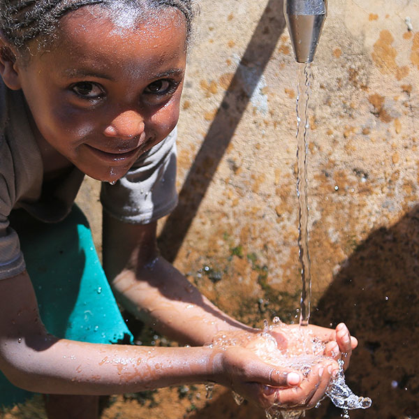Ein Kind schöpft mit seinen Händen frisches, sauberes Wasser aus einer Quellfassung.