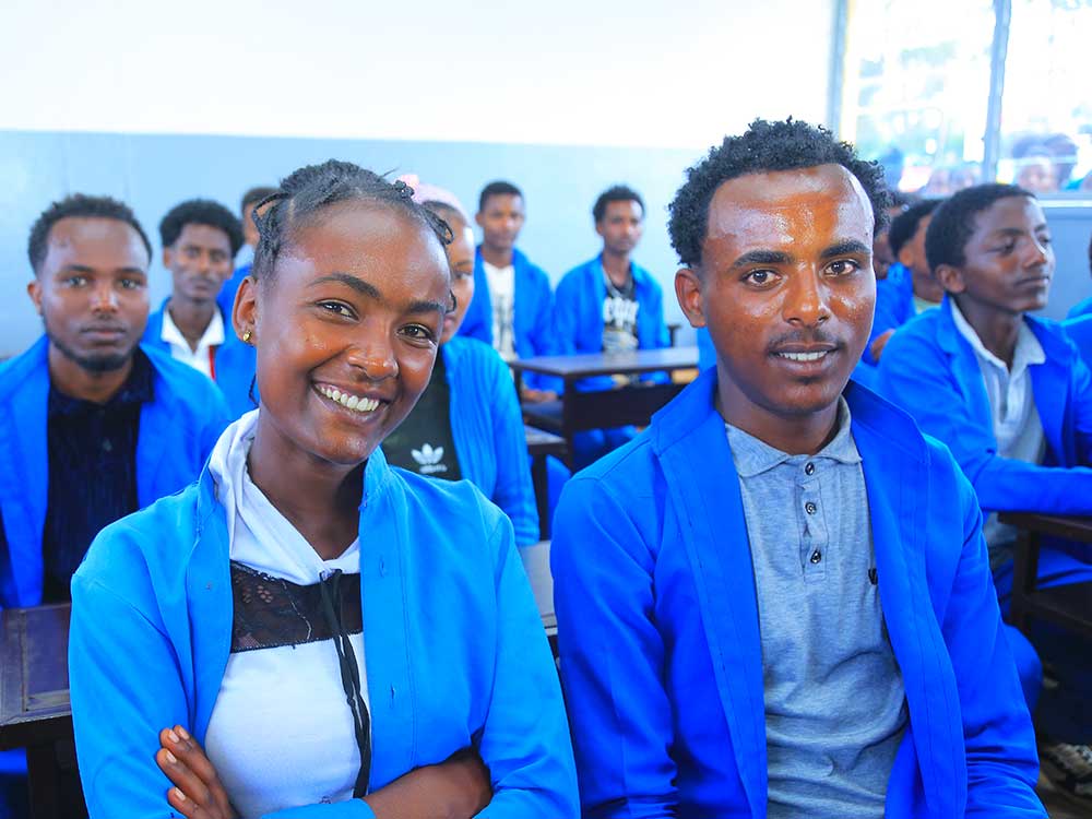 Kinder in blauen Schuluniformen sitzen auf Bänken im Klassenzimmer und lächeln in die Kamera.