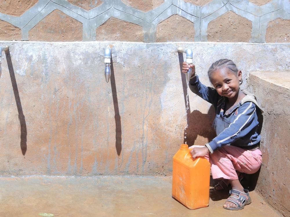 Ein Mädchen füllt an einer Quellfassung ihren gelben Wasserkanister mit frischem, sauberem Wasser.