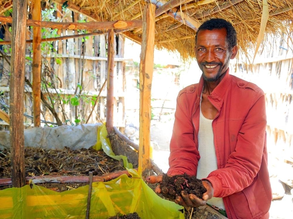 Ein Mann steht neben einem Wurmkomposter und hält Erde in seinen Händen.