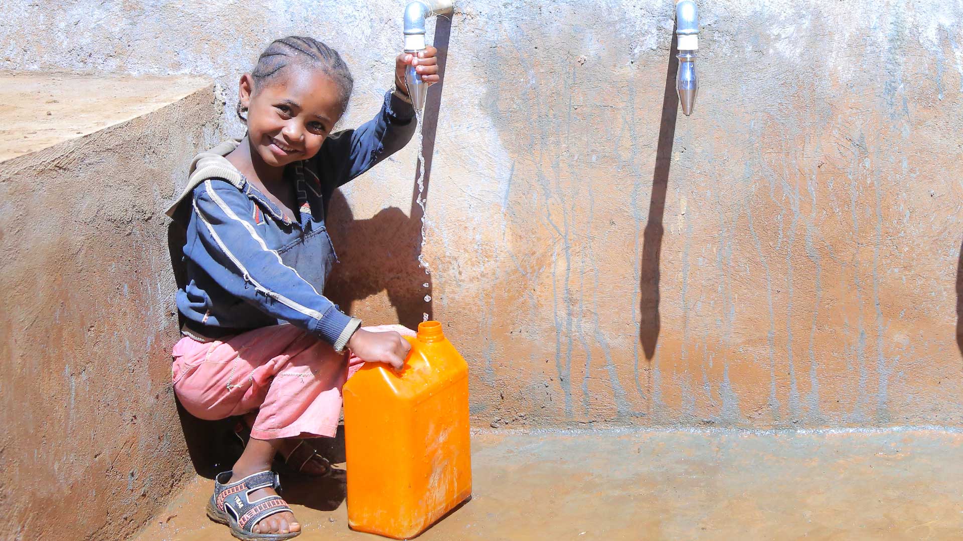 Eine Frau steht mit ihrem Kind auf dem Rücken vor einem Strauch und pflückt Früchte.