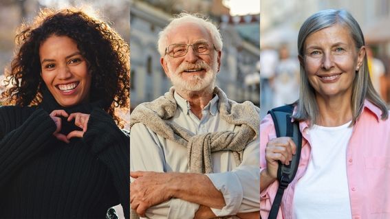 Drei lächelnde Personen unterschiedlichen Alters stehen nebeneinander, ganz links eine Frau mit lockigen dunklen Haaren, die mit den Händen ein Herz formt, in der Mitte ein älterer Mann mit weißen Haaren und Brille und ganz rechts eine ältere Frau mit grauen, schulterlangen Haaren. Alle drei lächeln in die Kamera