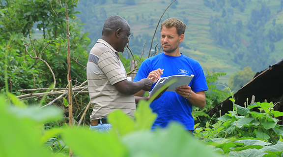 Markus Schwarz-Herda im blauen T-Shirt im Gespräch mit Projektleiter Berhanu Bedassa in einer grünen, hügeligen Landschaft in Äthiopien. Sie begutachten gemeinsam Unterlagen.