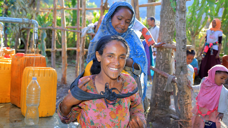 Eine Frau trägt auf dem Rücken einen gelben Wasserkanister.