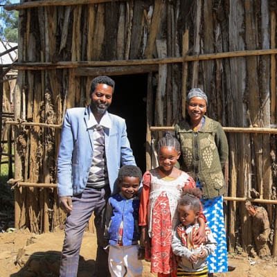 Mann mit Familie in Äthiopien steht vor seinem neuen Holzhäuschen