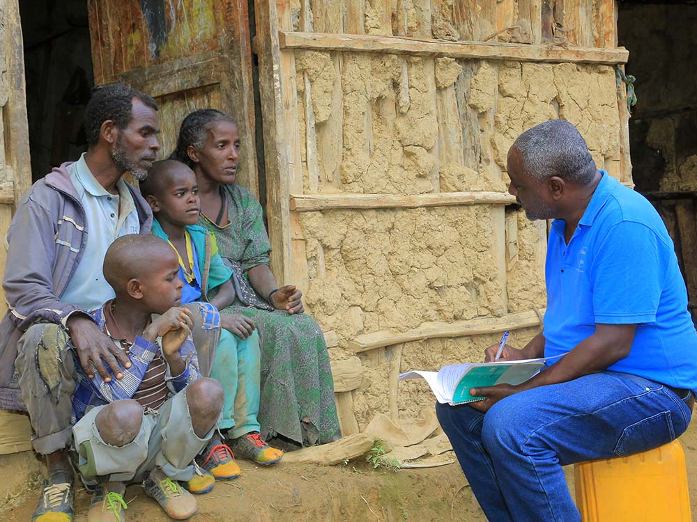 Eine äthiopische Familie - Vater, Mutter und 2 Söhne - sitzt mit MfM-Projektleiter Berhanu Bedassa vor ihrer Hütte und unterhält sich mit ihm