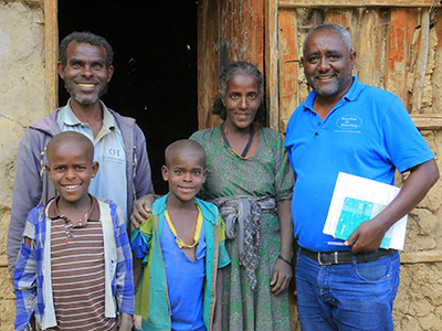 Eine äthiopische Familie - Vater, Mutter und 2 Söhne - steht mit MfM-Projektleiter Berhanu Bedassa vor ihrer Hütte