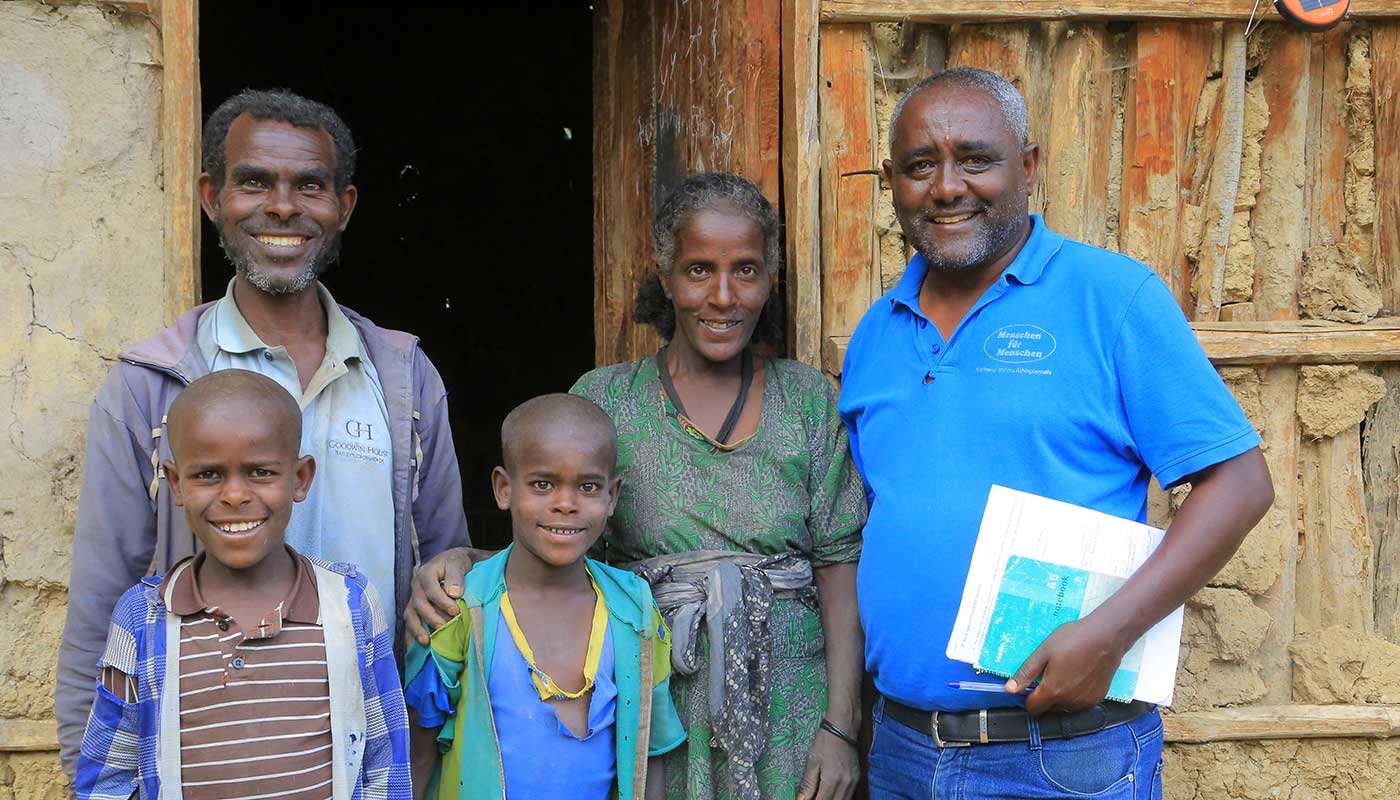 Eine äthiopische Familie - Vater, Mutter und 2 Söhne - steht mit MfM-Projektleiter Berhanu Bedassa vor ihrer Hütte