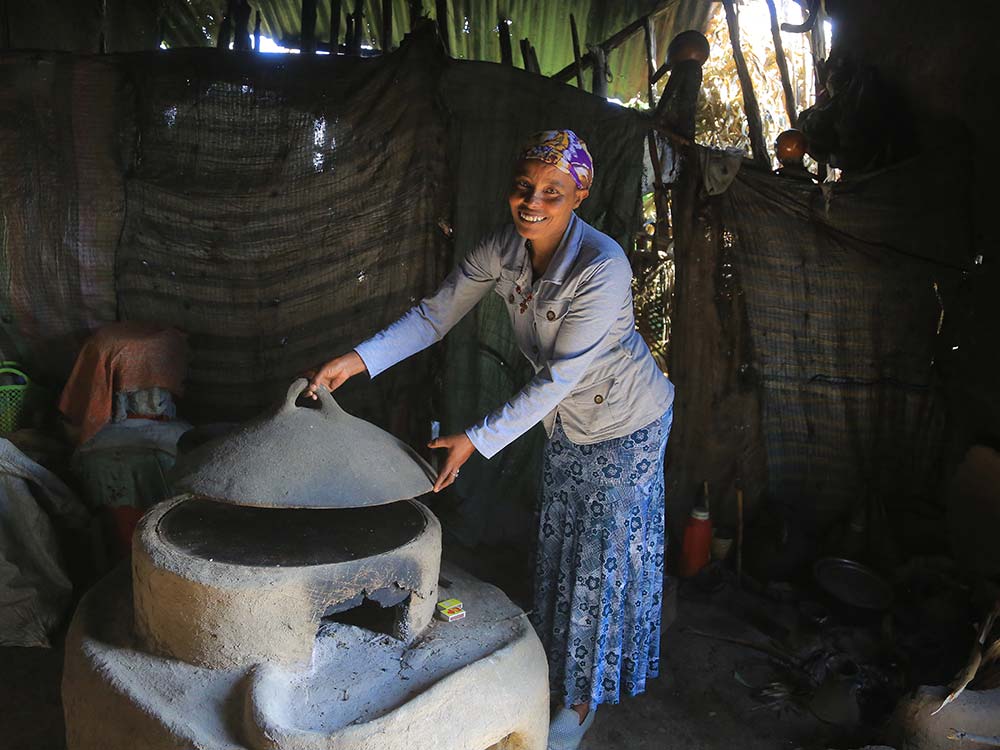 Eine äthiopische Frau hebt den Deckel ihres geschlossenen Ofens aus Beton an