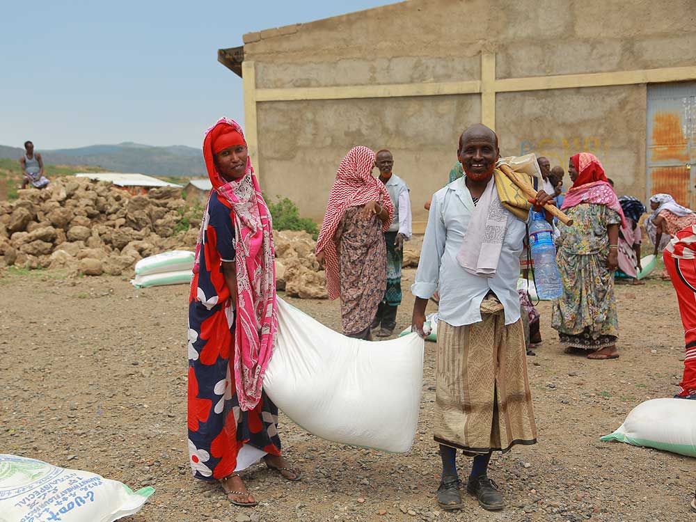 Eine Frau und ein Mann bei einer Nahrungsmittelausgabe in Äthiopien tragen einen Sack Getreide 