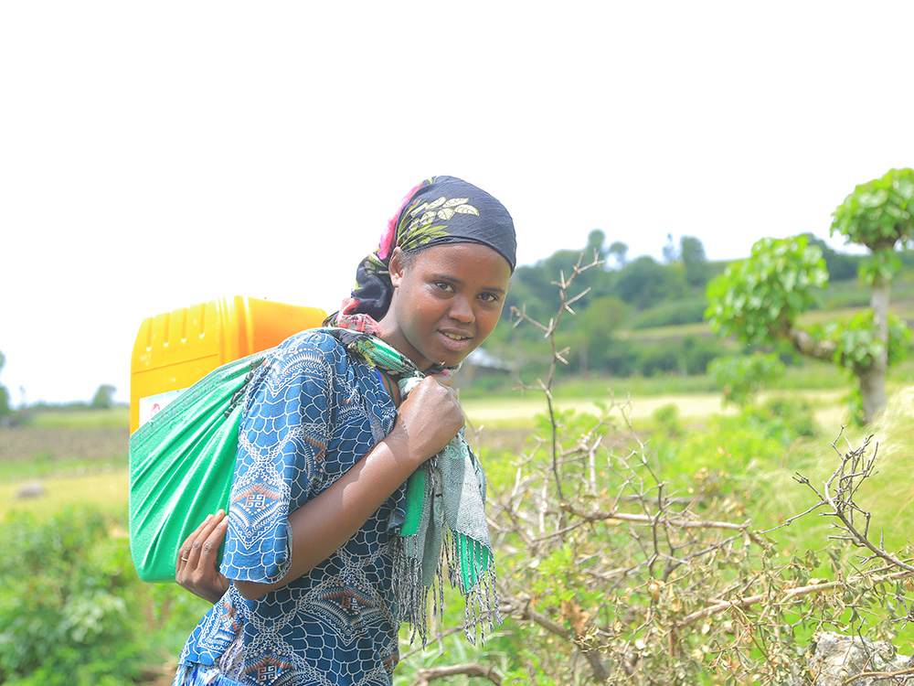 Ein äthiopisches Mädchen mit einem gelben Wasserkanister auf dem Rücken blickt in die Kamera