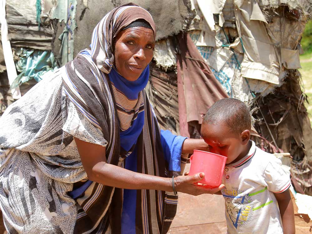 Nahaufnahme einer Mutter in Äthiopien, die ihrem Kind aus einem Plastikbecher etwas zu trinken gibt