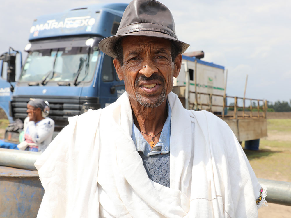 Ein alter Mann mit Hut steth vor einem LKW und blickt in die Kamera