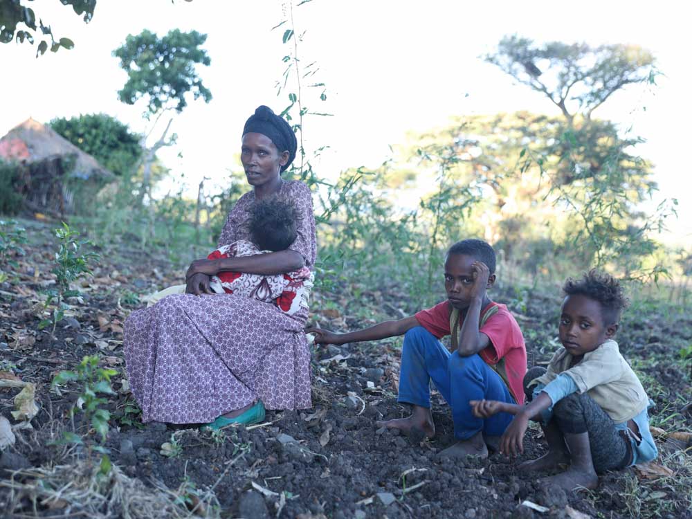 Mutter sitzt mit drei Kindern im Feld vor ihrer Hütte in Äthiopien