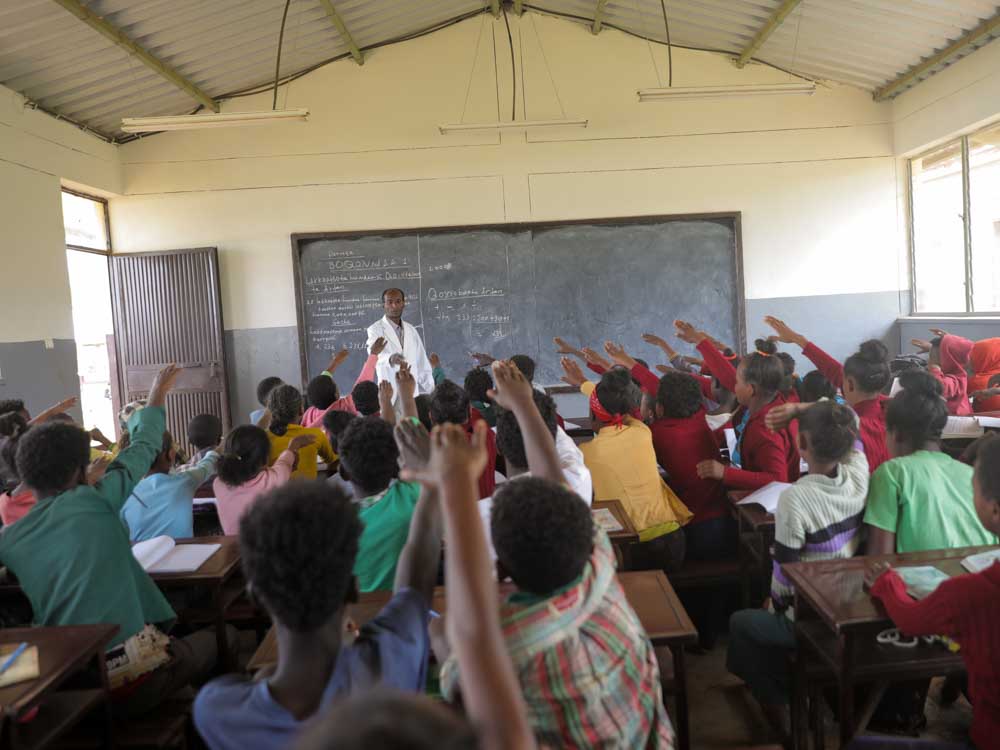 Schüler in neuer Schule in Äthiopien heben alle ihren Arm zum Lehrer