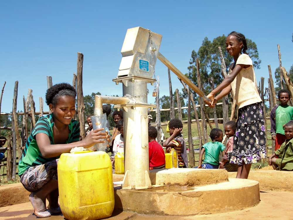 Zwei Mädchen mit einem gelben Kanister füllen Wasser aus einem Brunnen von Menschen für Menschen ab