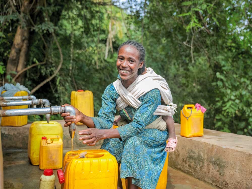 Frau in Äthiopien holt sauberes Trinkwasser aus einem Brunnen von Menschen für Menschen