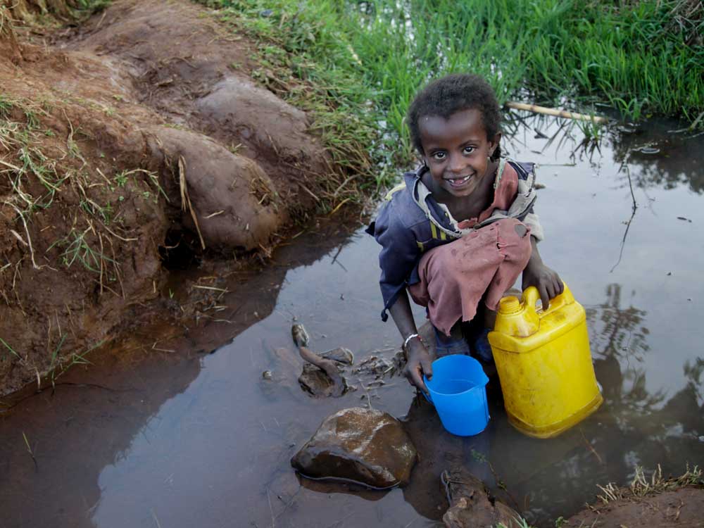 Ein äthiopisches Mädchen sitzt in einer dreckigen Lacke und schöpft verschmutztes Trinkwasser