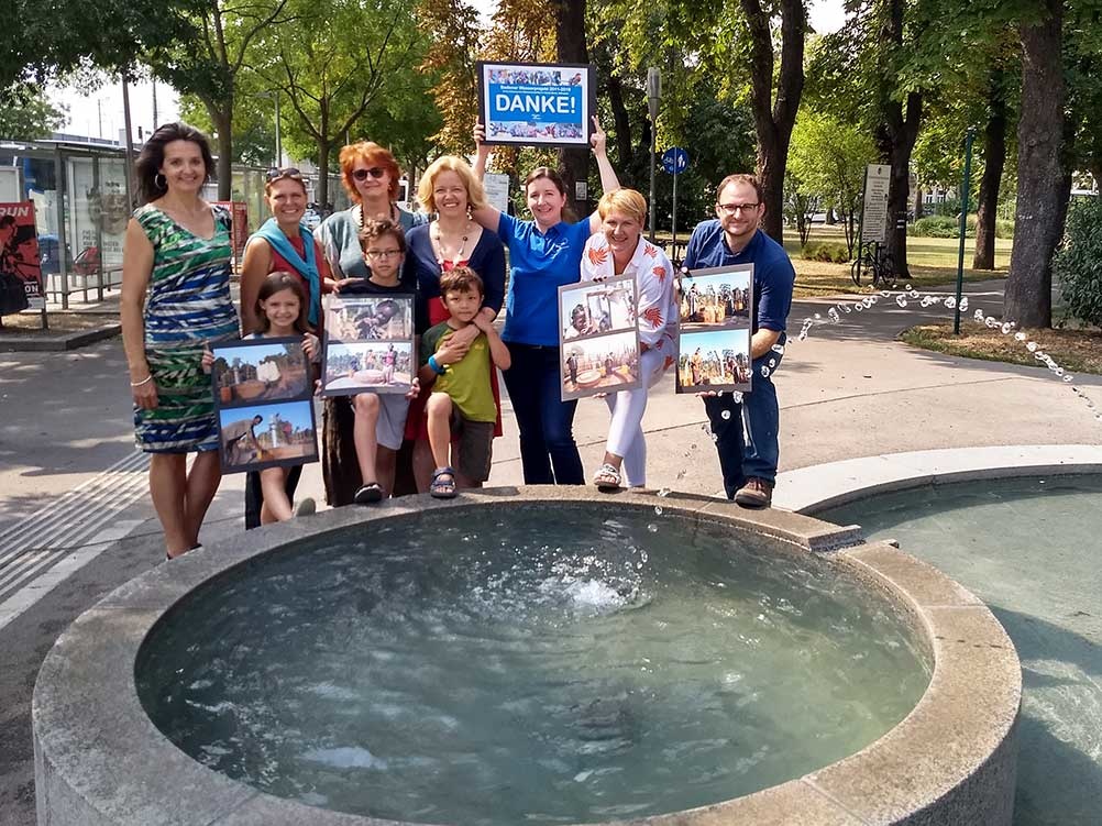 Menschen stehen vor einem Brunnen und halten Schilder auf denen Danke steht.