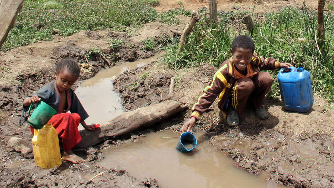 Zwei Kinder schöpfen Wasser aus einer Wasserstelle.
